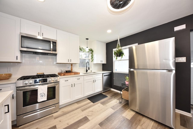 kitchen featuring sink, white cabinetry, decorative light fixtures, appliances with stainless steel finishes, and backsplash