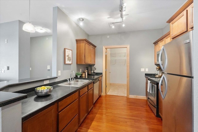 kitchen featuring appliances with stainless steel finishes, sink, light wood-type flooring, and decorative light fixtures