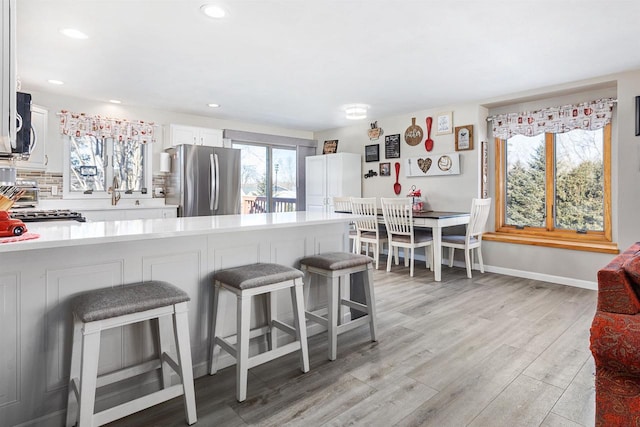 kitchen with a kitchen bar, white cabinetry, light wood-type flooring, stainless steel fridge, and stove