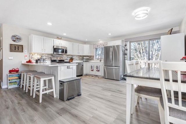 kitchen with a kitchen breakfast bar, stainless steel appliances, white cabinets, kitchen peninsula, and light wood-type flooring