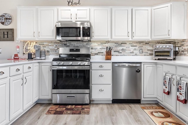 kitchen featuring appliances with stainless steel finishes, white cabinets, light wood-type flooring, and decorative backsplash