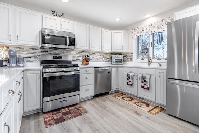 kitchen with tasteful backsplash, appliances with stainless steel finishes, white cabinets, and light wood-type flooring