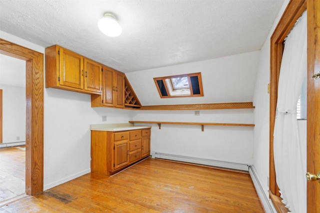 kitchen featuring a baseboard heating unit, vaulted ceiling with skylight, light hardwood / wood-style floors, and a textured ceiling