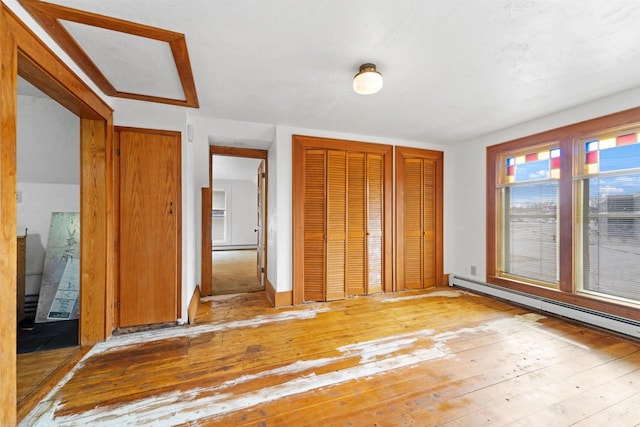 unfurnished bedroom with baseboard heating, multiple closets, and light wood-type flooring