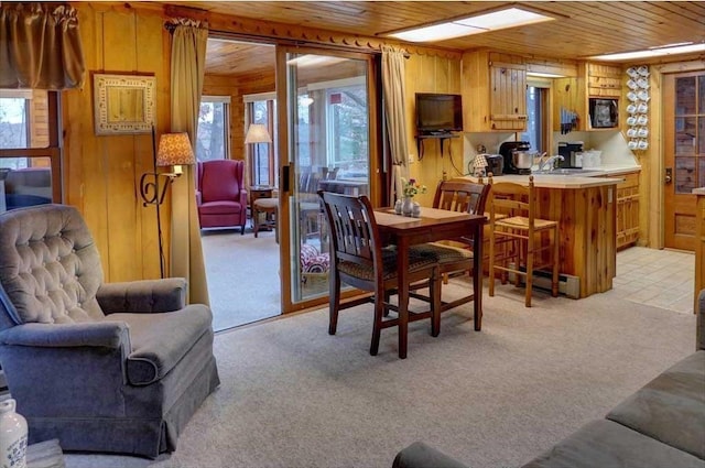 dining area featuring sink, light colored carpet, wooden ceiling, and wood walls