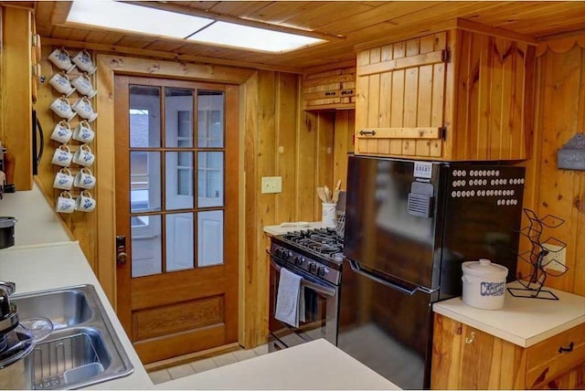 kitchen featuring sink, wood walls, wood ceiling, black refrigerator, and stainless steel range with gas stovetop