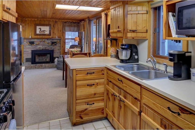 kitchen with black refrigerator, a fireplace, sink, light colored carpet, and wooden ceiling