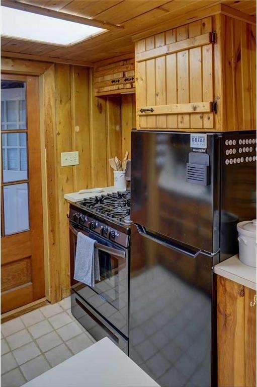 kitchen with black refrigerator, range with gas stovetop, wood ceiling, and wood walls