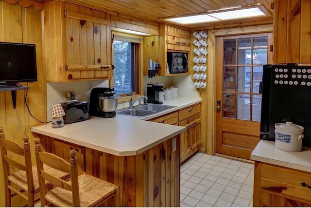 kitchen with sink, black fridge, light tile patterned floors, wooden ceiling, and kitchen peninsula