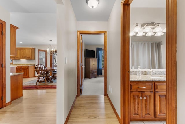 corridor with sink, a notable chandelier, and light wood-type flooring