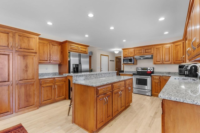 kitchen featuring sink, a center island, light wood-type flooring, appliances with stainless steel finishes, and light stone countertops