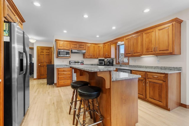 kitchen with appliances with stainless steel finishes, a kitchen breakfast bar, a center island, light hardwood / wood-style floors, and light stone countertops