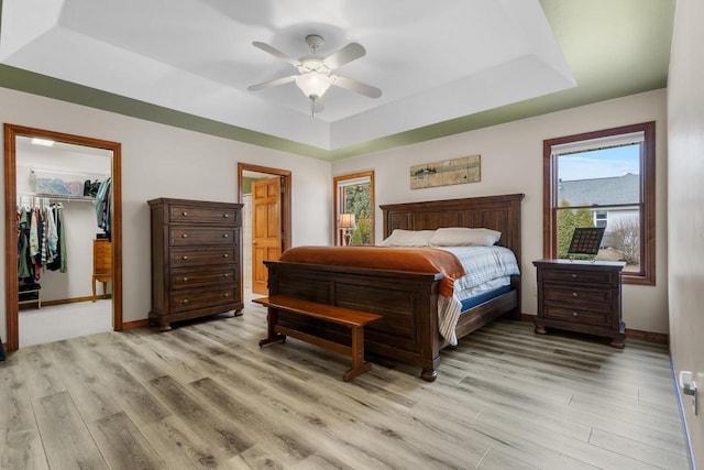 bedroom with light hardwood / wood-style flooring, ceiling fan, a raised ceiling, a spacious closet, and a closet