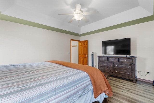 bedroom with a raised ceiling, ceiling fan, and light wood-type flooring