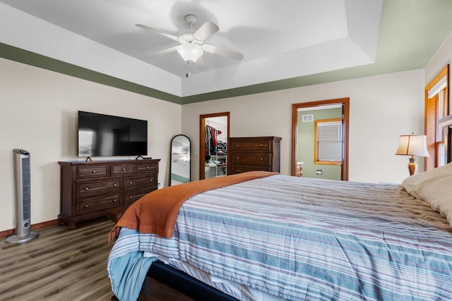 bedroom featuring a closet, ceiling fan, dark hardwood / wood-style flooring, a walk in closet, and a raised ceiling