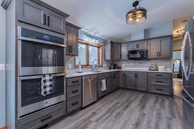 kitchen with vaulted ceiling, appliances with stainless steel finishes, sink, decorative backsplash, and light hardwood / wood-style flooring