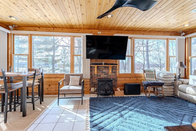 tiled living room featuring plenty of natural light, a wood stove, wooden ceiling, and wood walls