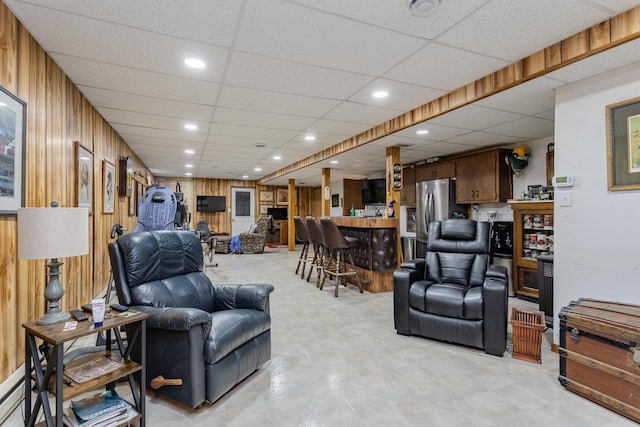 living room featuring indoor bar, a drop ceiling, and wooden walls