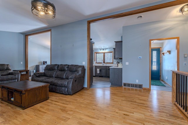 living room featuring sink, vaulted ceiling, and light wood-type flooring