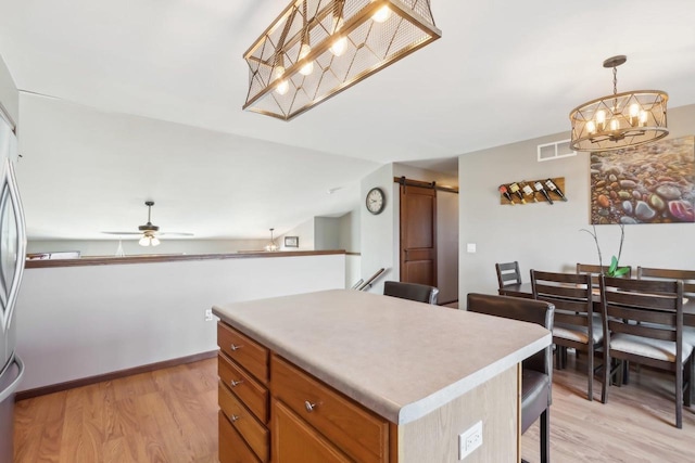 kitchen featuring a kitchen island, ceiling fan with notable chandelier, hanging light fixtures, a barn door, and light wood-type flooring