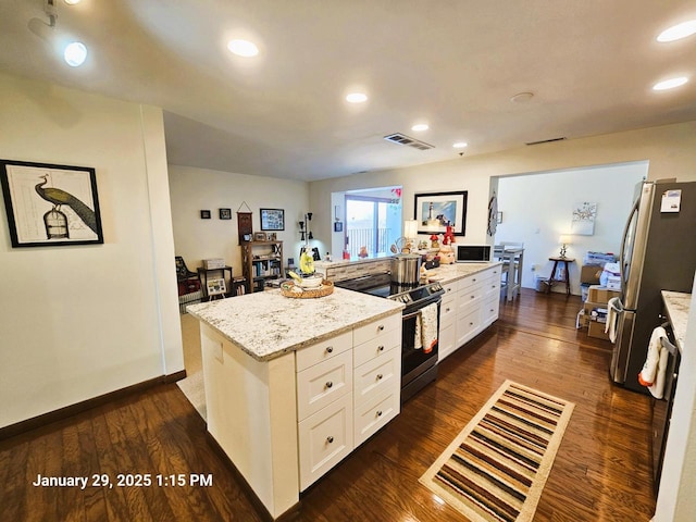 kitchen with electric range oven, stainless steel fridge, white cabinets, a center island, and light stone counters