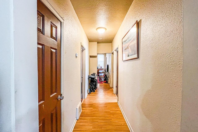 hallway with light hardwood / wood-style floors and a textured ceiling