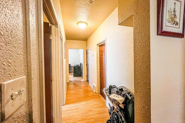 hall featuring light hardwood / wood-style floors and a textured ceiling