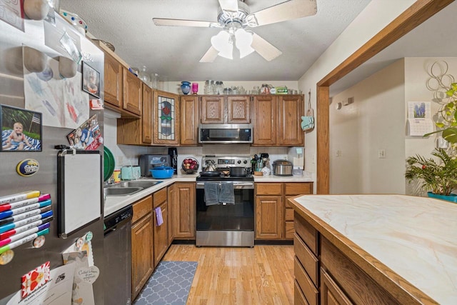 kitchen featuring appliances with stainless steel finishes, sink, light wood-type flooring, ceiling fan, and a textured ceiling