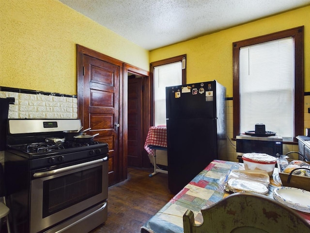 kitchen with stainless steel gas stove, dark hardwood / wood-style floors, a textured ceiling, and black fridge