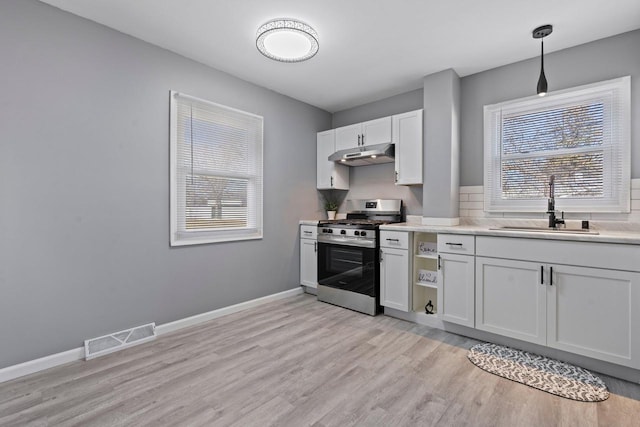 kitchen featuring sink, white cabinetry, stainless steel range with gas stovetop, decorative light fixtures, and light wood-type flooring