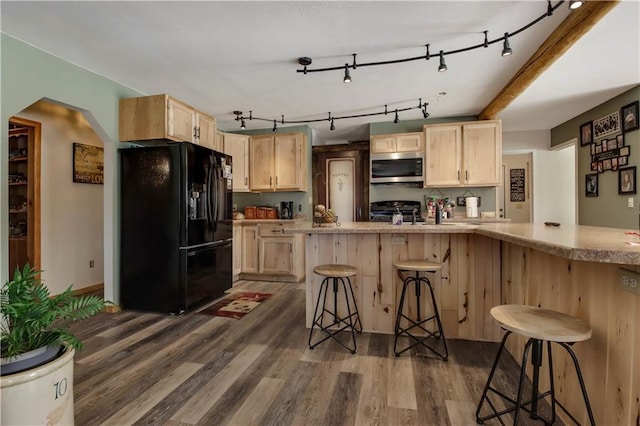 kitchen with light brown cabinetry, black fridge, dark hardwood / wood-style floors, a kitchen breakfast bar, and kitchen peninsula