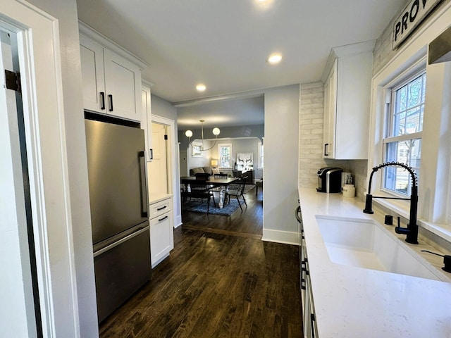 kitchen featuring sink, dark wood-type flooring, stainless steel refrigerator, light stone counters, and white cabinets