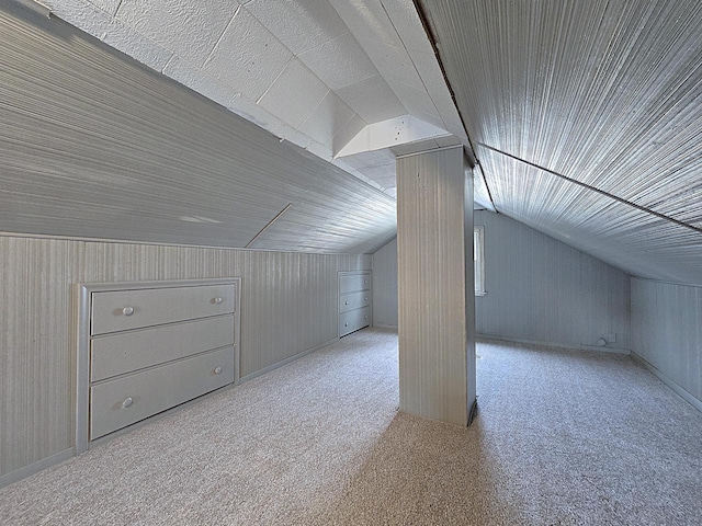 additional living space with vaulted ceiling, light carpet, and wood walls