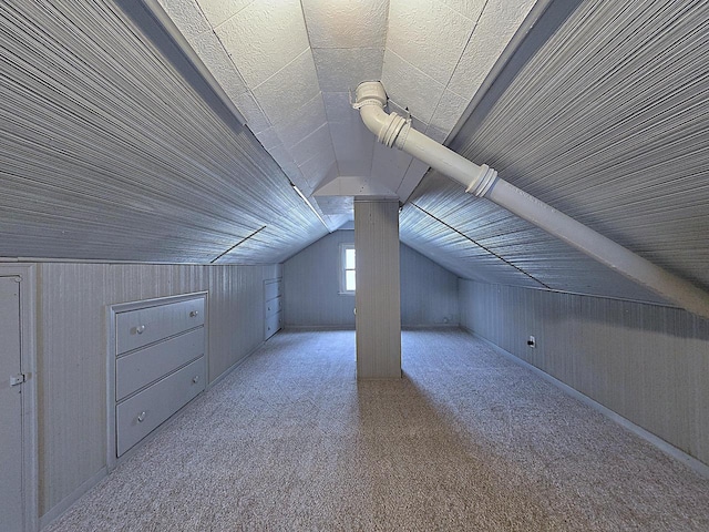 additional living space featuring vaulted ceiling, light colored carpet, and wood walls