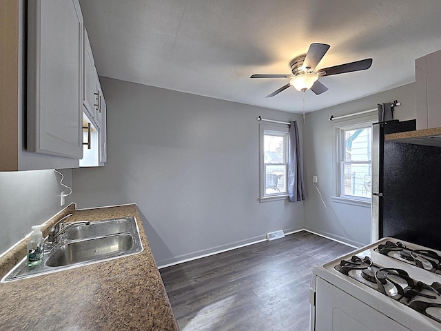 kitchen featuring stainless steel refrigerator, white gas range, sink, white cabinets, and dark wood-type flooring