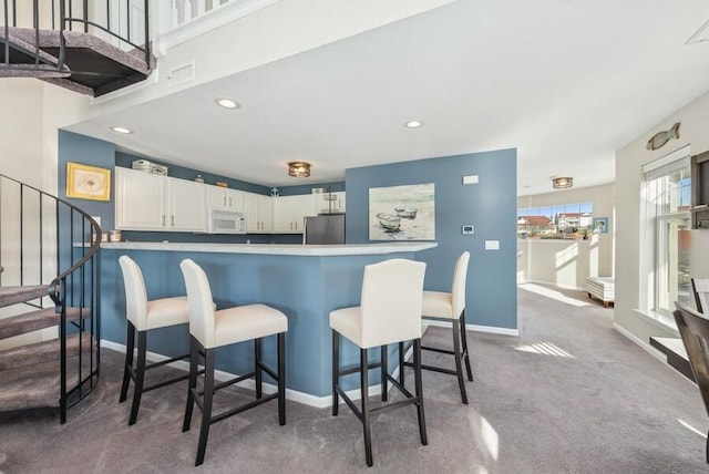 kitchen featuring stainless steel refrigerator, white cabinetry, carpet floors, a kitchen bar, and kitchen peninsula