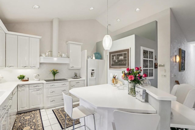 kitchen with a breakfast bar, vaulted ceiling, pendant lighting, white refrigerator with ice dispenser, and white cabinets