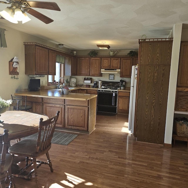 kitchen featuring dark wood-type flooring, sink, gas range, white refrigerator, and kitchen peninsula