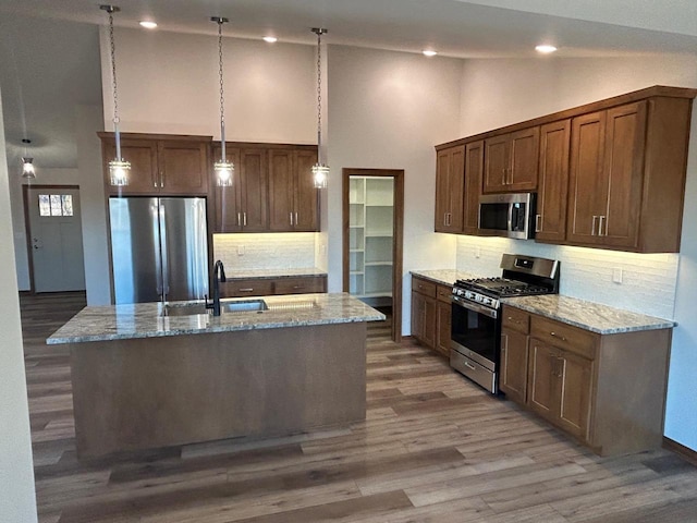 kitchen with light stone counters, appliances with stainless steel finishes, decorative light fixtures, and a center island with sink