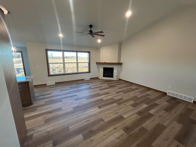 unfurnished living room with dark hardwood / wood-style floors, ceiling fan, and a stone fireplace