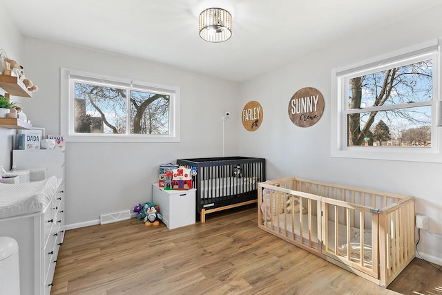 bedroom with multiple windows, a nursery area, and hardwood / wood-style floors