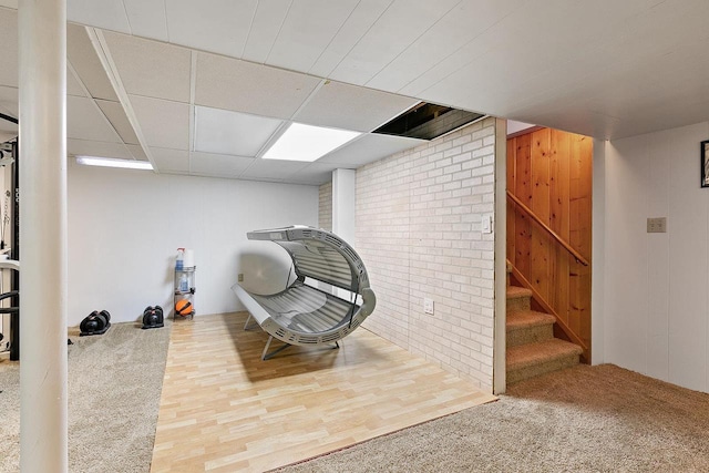 living area with wood walls, brick wall, and a drop ceiling