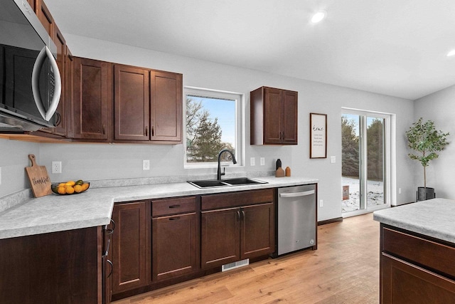 kitchen featuring stainless steel appliances, sink, dark brown cabinetry, and light wood-type flooring