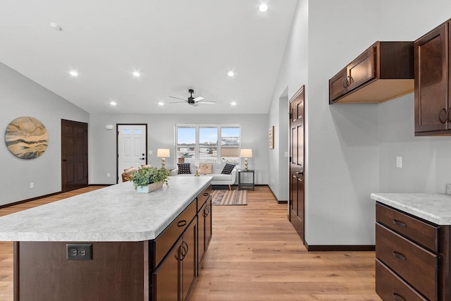 kitchen with lofted ceiling, ceiling fan, dark brown cabinets, a center island, and light hardwood / wood-style floors