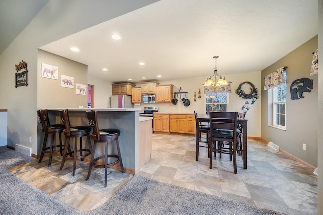 kitchen featuring a breakfast bar, light brown cabinetry, decorative light fixtures, appliances with stainless steel finishes, and a notable chandelier