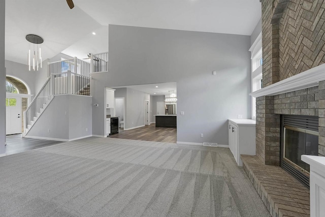 unfurnished living room with dark colored carpet, a brick fireplace, an inviting chandelier, and high vaulted ceiling