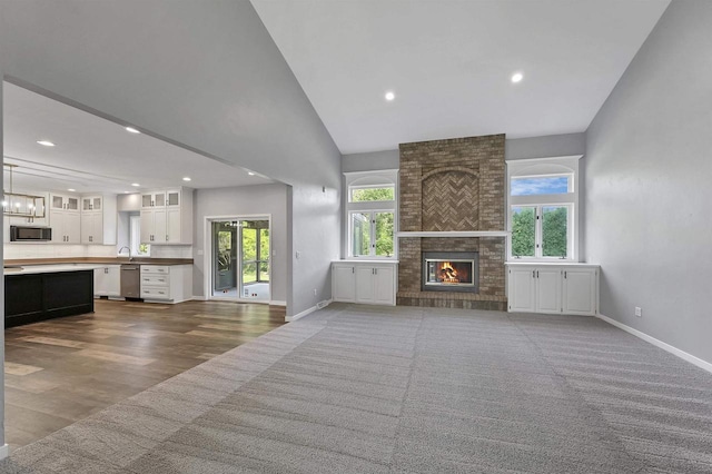 unfurnished living room featuring wood-type flooring, sink, high vaulted ceiling, and a brick fireplace