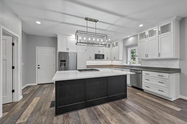 kitchen with appliances with stainless steel finishes, dark hardwood / wood-style floors, white cabinetry, hanging light fixtures, and a center island