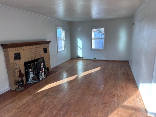 unfurnished living room featuring crown molding, wood-type flooring, a brick fireplace, and plenty of natural light