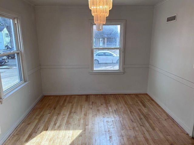 unfurnished dining area featuring ornamental molding, a healthy amount of sunlight, a chandelier, and light wood-type flooring